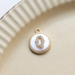 Detail of round gold-plated pendant with mother of pearl and zircon letter Q on ceramic