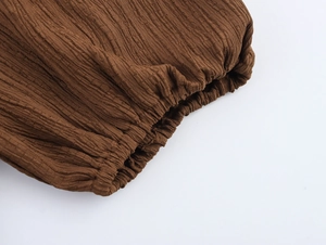 Detailed close-up of brown textured fabric with smocked elastic cuff and pleated finish