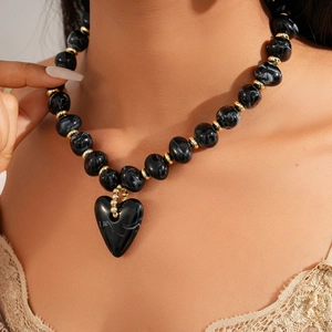 Close-up of black beaded necklace with a heart pendant on a model's neck for winter styling