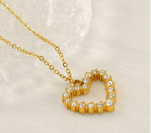 Detailed close-up of a golden heart necklace with crystals on a textured white fabric