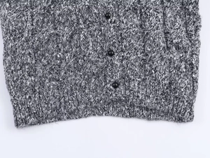 Détail de maille torsadée avec boutons noirs et bord-côte sur un cardigan en tricot gris