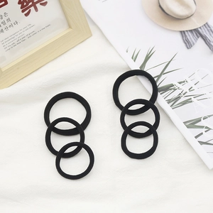Detail of six black seamless high-elastic hair ties on a textured white fabric background