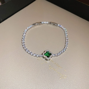 Detail of silver tennis bracelet featuring emerald clover charm and white zircon inlay
