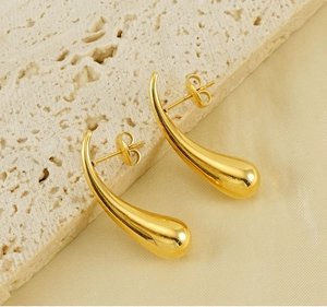 Macro view of polished gold teardrop earrings resting on champagne silk and textured stone