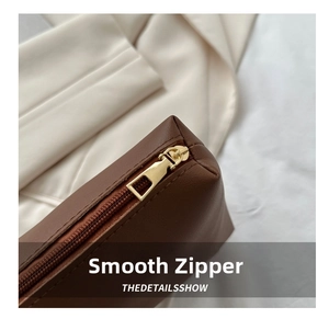 Close-up of smooth gold metal zipper and brown litchi grain leather texture