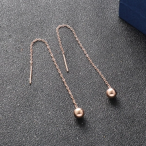 Orecchini a goccia con sfera in oro rosa 18K e catena lunga su superficie nera