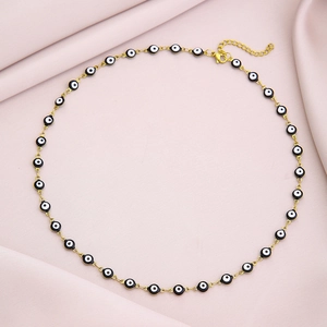 Gold evil eye necklace with black and white beads on soft pink fabric background