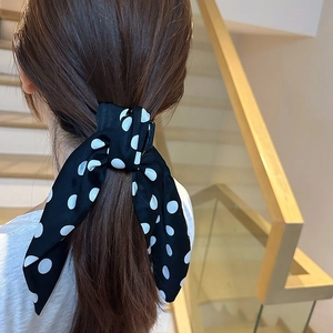 Close-up of a black silk bow hair clip with white polka dots worn on a ponytail