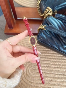 Detail of elegant gold oval watch with red crocodile leather strap held by a model