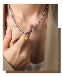 Detail of beaded stone necklace with gold oval Virgin Mary relief pendant on a model