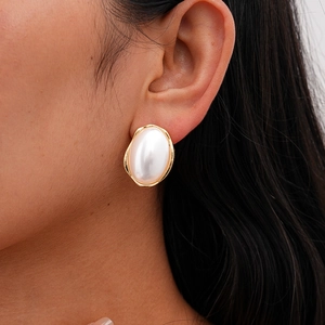Gros plan sur boucle d'oreille ovale dorée à bords ondulés et grosse perle blanche
