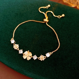 Detail of gold-plated clover bracelet with cat-eye stone petals on green velvet background