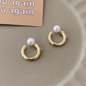 Detail of C-shaped gold metal earrings featuring white pearls on a textured plate