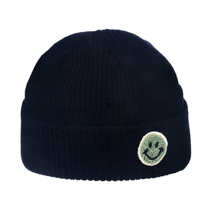 Detail of black ribbed knit beanie with a green fuzzy smiley face patch on the folded brim