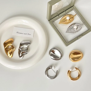 Elegant gold and silver stainless steel brooch collection with pearls on a modern display
