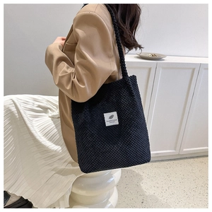 Detail of black waffle-textured tote bag with white letter patch on side view