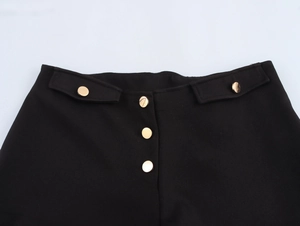 Close-up of low-rise black hot pants featuring decorative gold buttons and pocket flaps