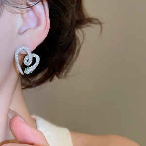Close-up of snake-shaped heart stud earrings with sparkling crystals and green eyes
