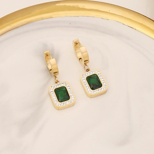 Detail of gold huggie earrings with square emerald zircon pendants on marble tray