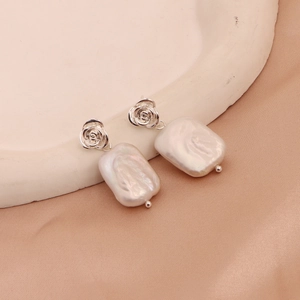 Close-up of baroque freshwater pearl earrings with silver rose flower stud design