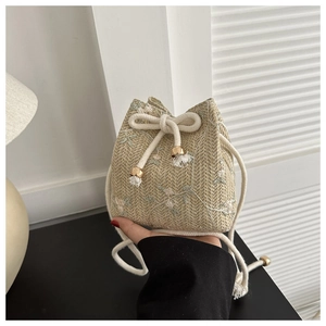 Detail of beige straw bucket bag featuring green flower embroidery and drawstring closure