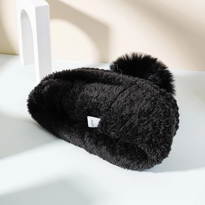 Detail of black knit beanie featuring thick plush lining and soft faux fur pom-pom