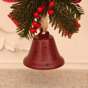 Close-up of a rustic dark red metal bell with red berries and greenery on a festive branch