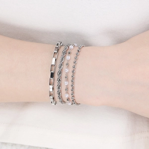 Detail of layered silver bracelets featuring a pearl charm and geometric metal chains