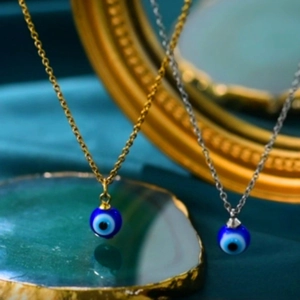 Close-up of gold and silver stainless steel evil eye charm necklaces on green background
