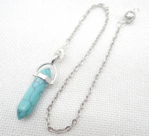 Detail of turquoise hexagonal prism pendant with silver metallic bail on white fabric