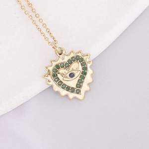 Detailed macro of gold heart pendant with blue eye and green crystal accents