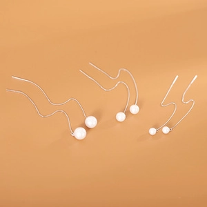 Detailed view of three pairs of silver wavy pearl earrings in small to large sizes