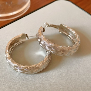 Macro shot of silver twisted hoop earrings with woven texture on a grey leather surface
