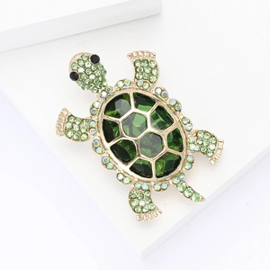 Cute green crystal turtle brooch with gold finish displayed on a white step background