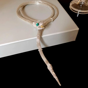 Detailed view of silver mesh snake necklace with green gemstone eyes on display box