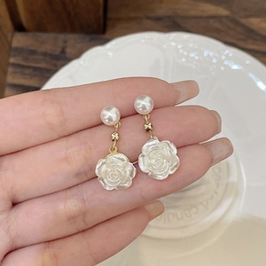 Close-up of French vintage rose and pearl earrings held over a white embossed ceramic plate