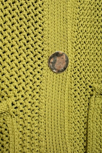 Macro shot of yellow-green knit texture and patterned metal button detail on the cardigan