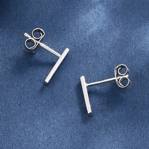 Macro shot of minimalist silver T-bar stud earrings on dark blue textured background
