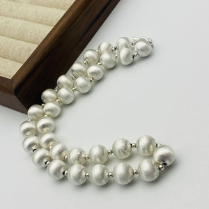 Détail du collier à billes argentées avec texture en métal brossé sur fond blanc