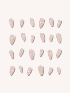 Macro detail of nude almond false nails featuring silver starburst patterns and matte finish