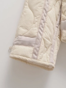 Close-up of quilted jacket cuff with decorative ribbon trim and fine stitching detail
