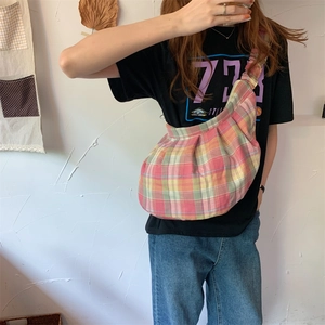 Detailed view of pink checkered canvas dumpling bag worn by a model in a casual setting