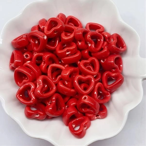 Close-up of red heart-shaped ink-wash ceramic beads piled in a white petal bowl