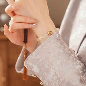 Detail of white crystal beaded bracelet with golden clover charm on a model's wrist