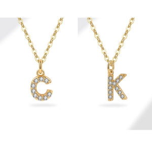Close-up of golden alphabet pendants C and K with zircon inlay on a white background