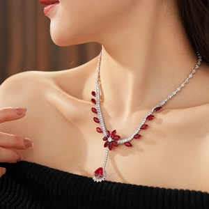 Close-up of a silver necklace featuring a red floral pendant and teardrop gemstone on model