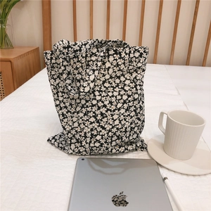 Detailed close-up of a black canvas tote bag with white floral pattern on a white bed