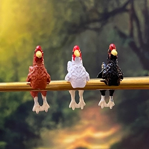 Dettaglio di tre statuine di gallo in miniatura in resina sedute su un bastone di legno