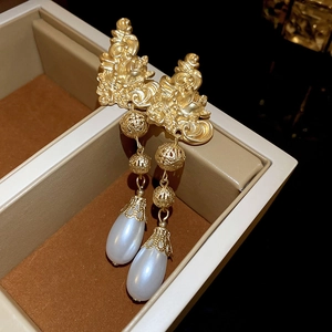 Detail of vintage gold flower earrings with teardrop pearls on a brown jewelry box lining