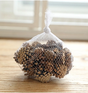 Close-up of natural brown pine cones in a white mesh bag on a warm wooden surface